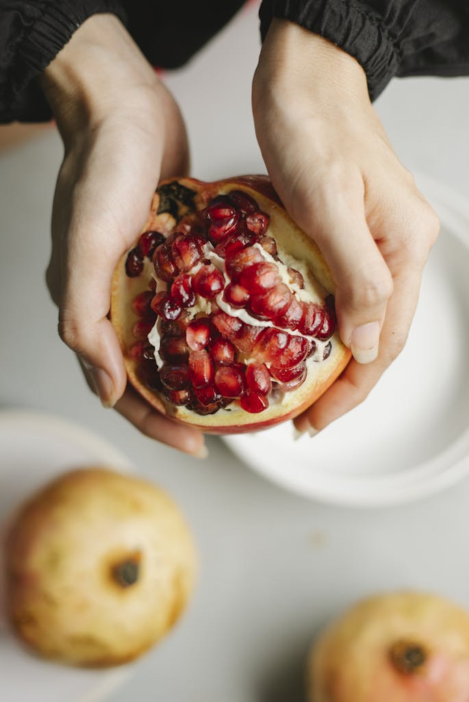 Hands holding a ripe pomegranate revealing juicy seeds. Perfect for healthy lifestyle visuals.